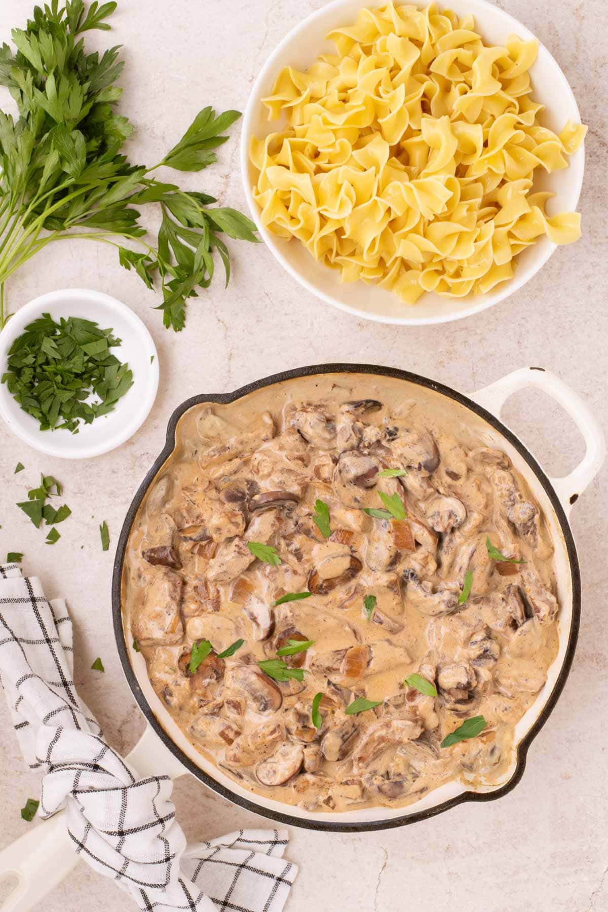 Overhead shot of beef stroganoff in a skillet next to parsley and egg noodles.