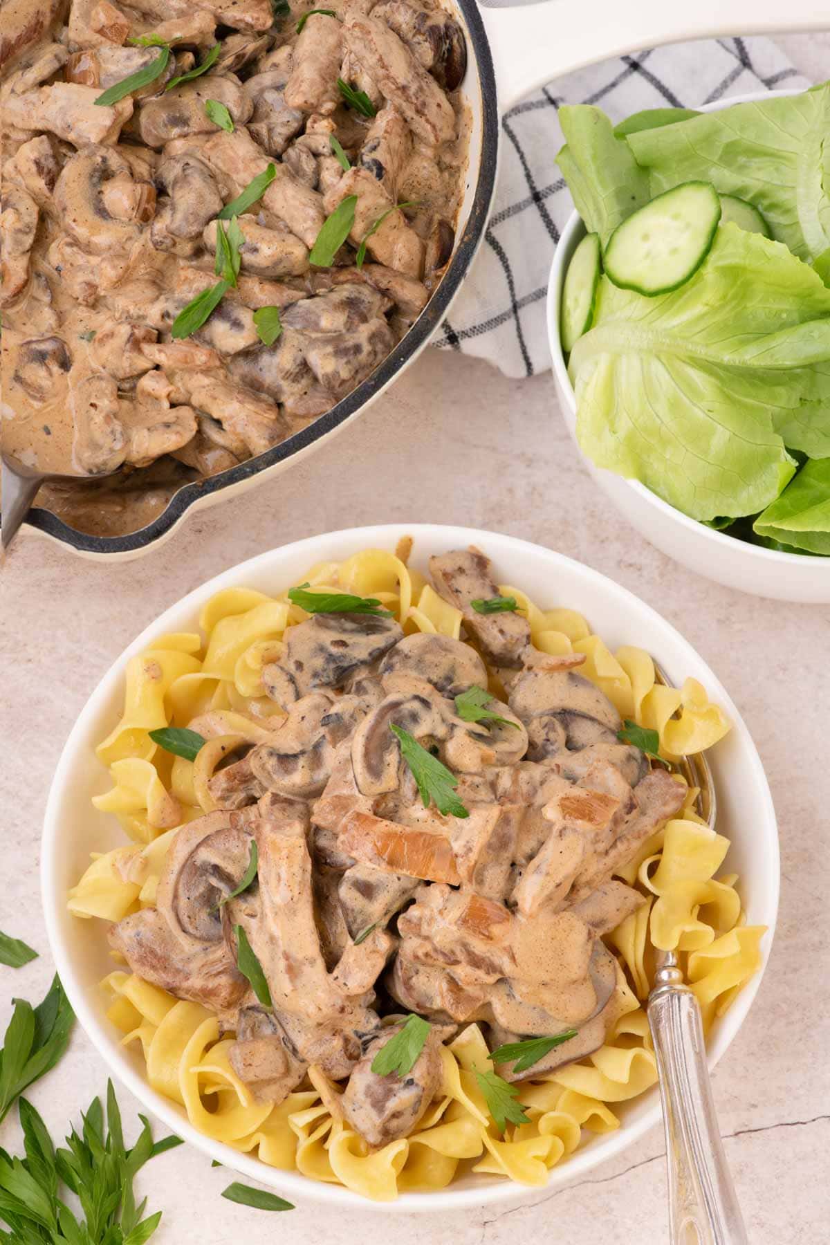 Beef stroganoff served over a bed of egg noodles in a bowl.