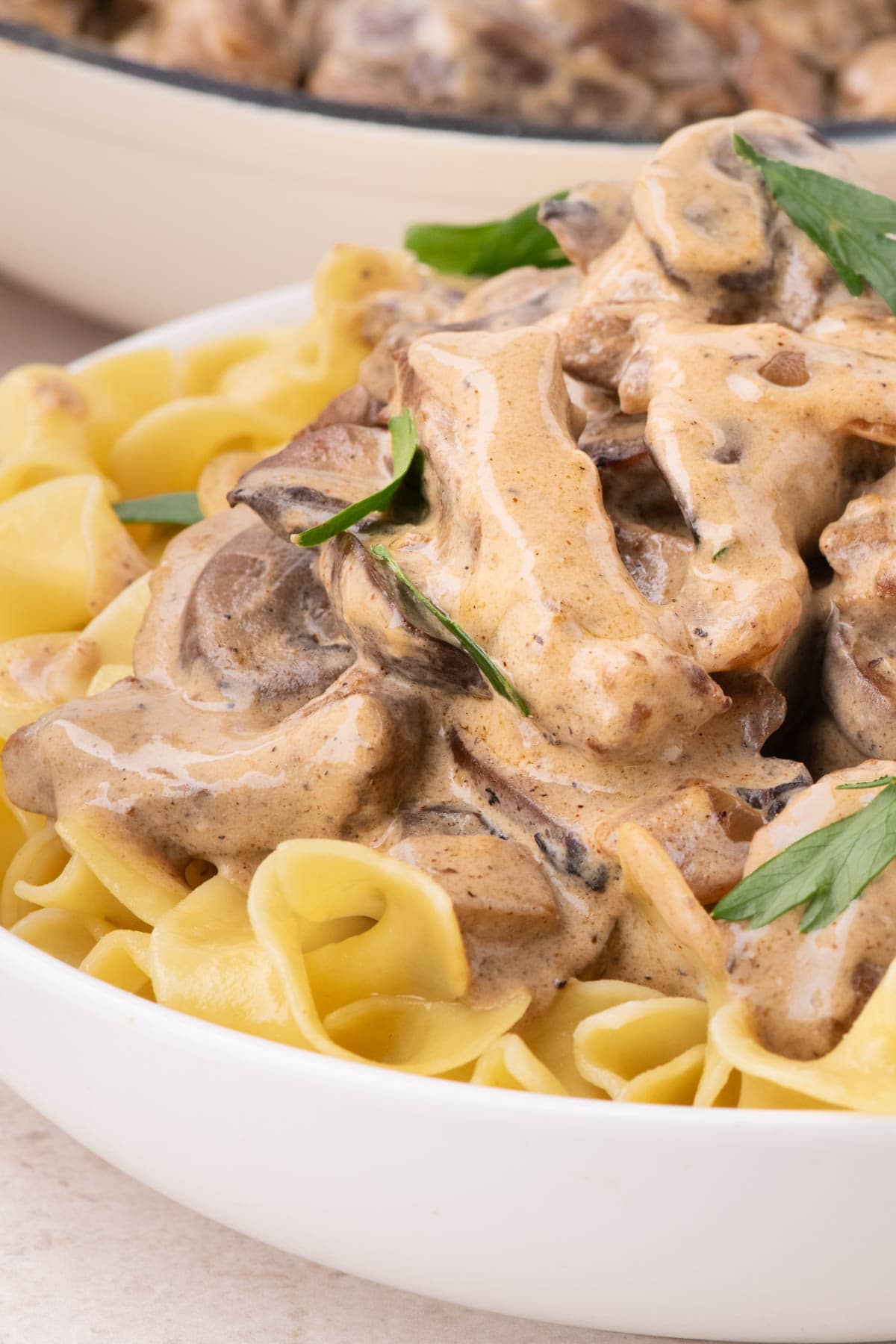 White bowl with egg noodles topped with beef stroganoff and fresh parsley.