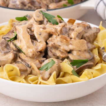 A white bowl filled with egg noodles topped with creamy beef stroganoff.