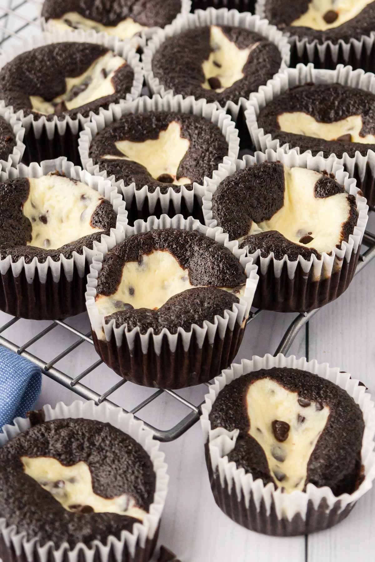 Chocolate cupcakes with a cheesecake filling on a cooling rack.