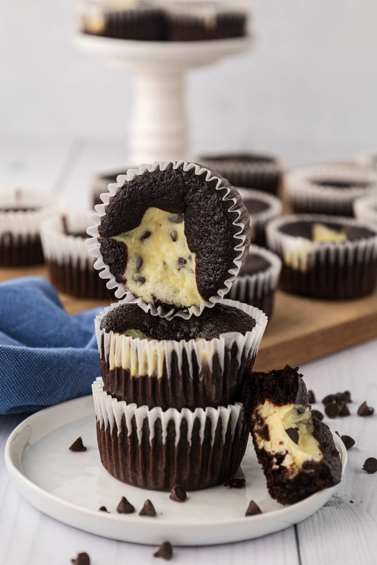 Three black bottom cupcakes stacked on a white plate with half of a cupcake cut open so you can see the inside.