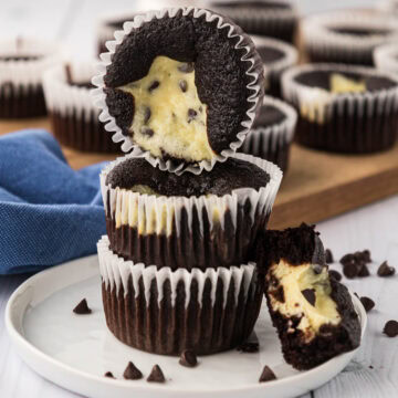 Three black bottom cupcakes stacked on a white plate with half of a cupcake cut open so you can see the inside.