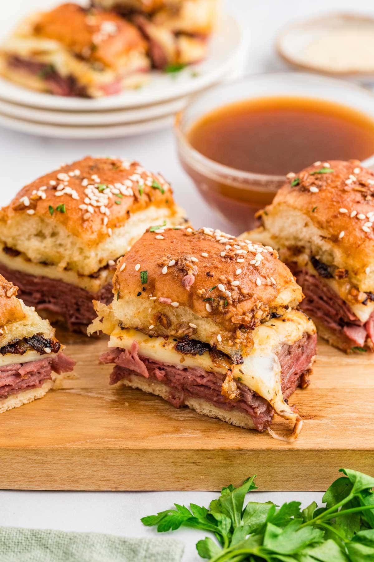 Four French dip sliders served on a wooden board with a dipping sauce in the background.