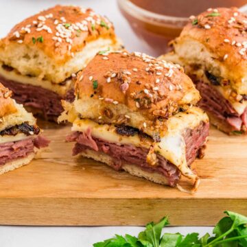 French dip sliders served on a wooden cutting board.