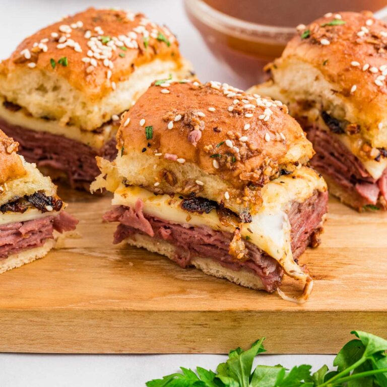 French dip sliders served on a wooden cutting board.