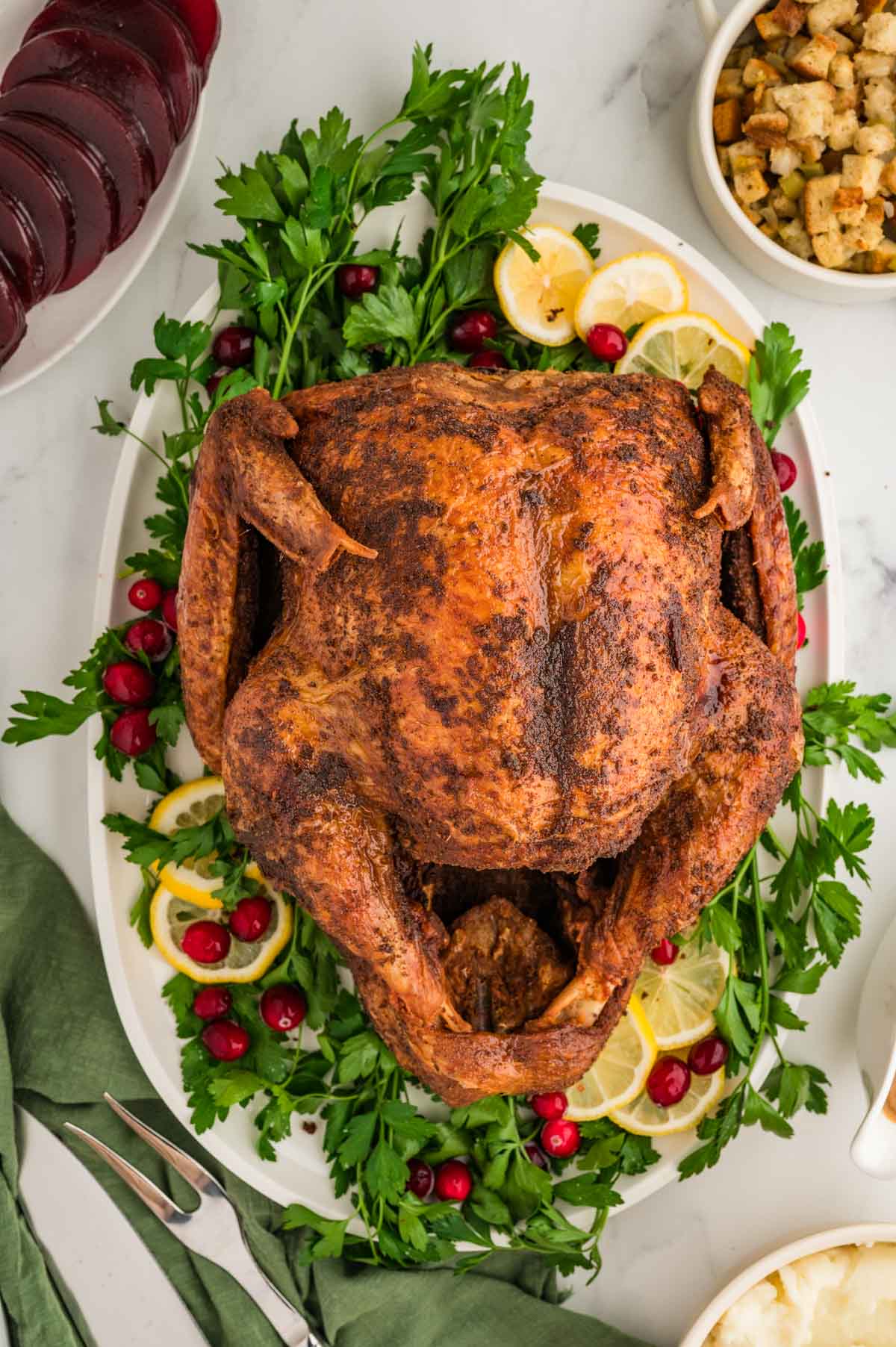 An overhead image of a whole deep fried turkey on a serving plate and garnished with cranberries and parsley.