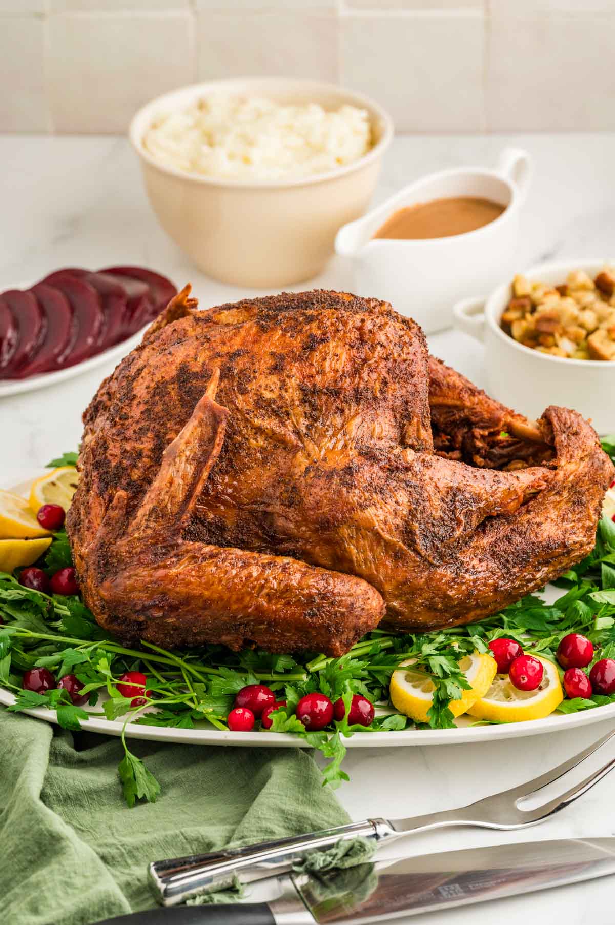 A deep fried turkey set on a white serving platter garnished with parsley, lemon slices, and fresh cranberries.