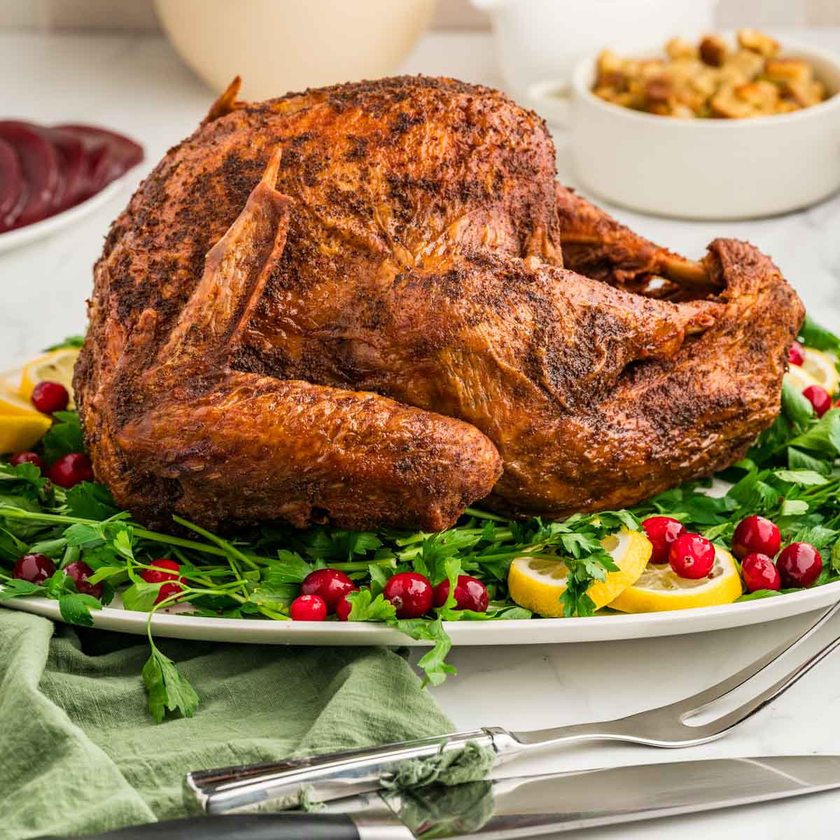 A deep fried turkey set on a white serving platter garnished with parsley, lemon slices, and fresh cranberries.