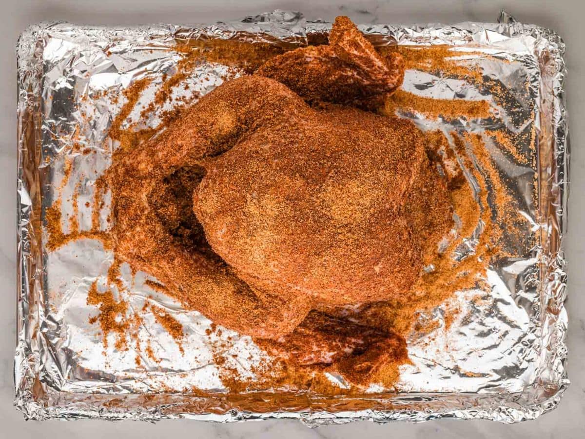 A turkey seasoned with cajun seasoning on a foil lined rimmed baking sheet.