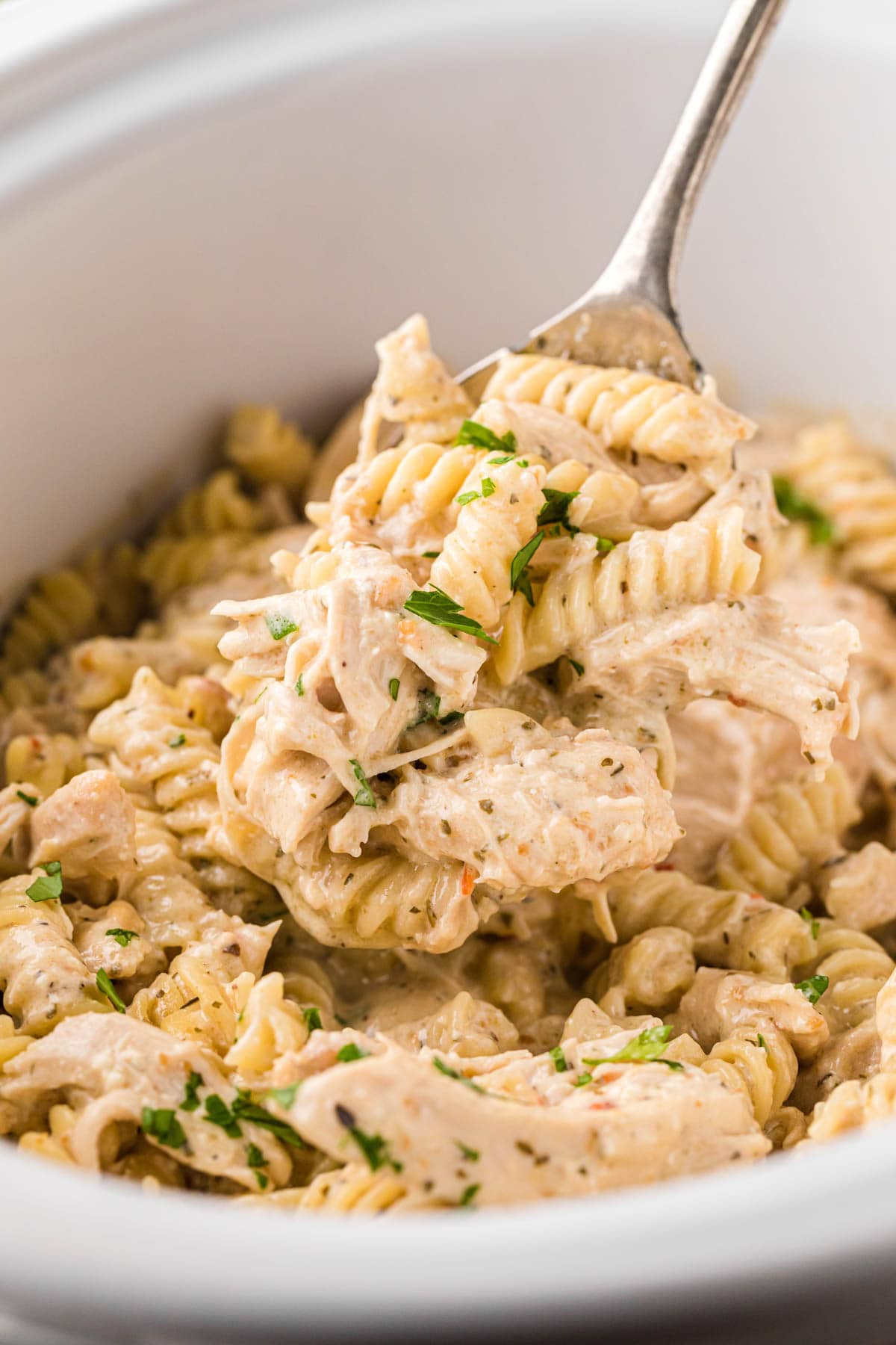 Scooping a spoonful of creamy chicken pasta out of the crock pot.