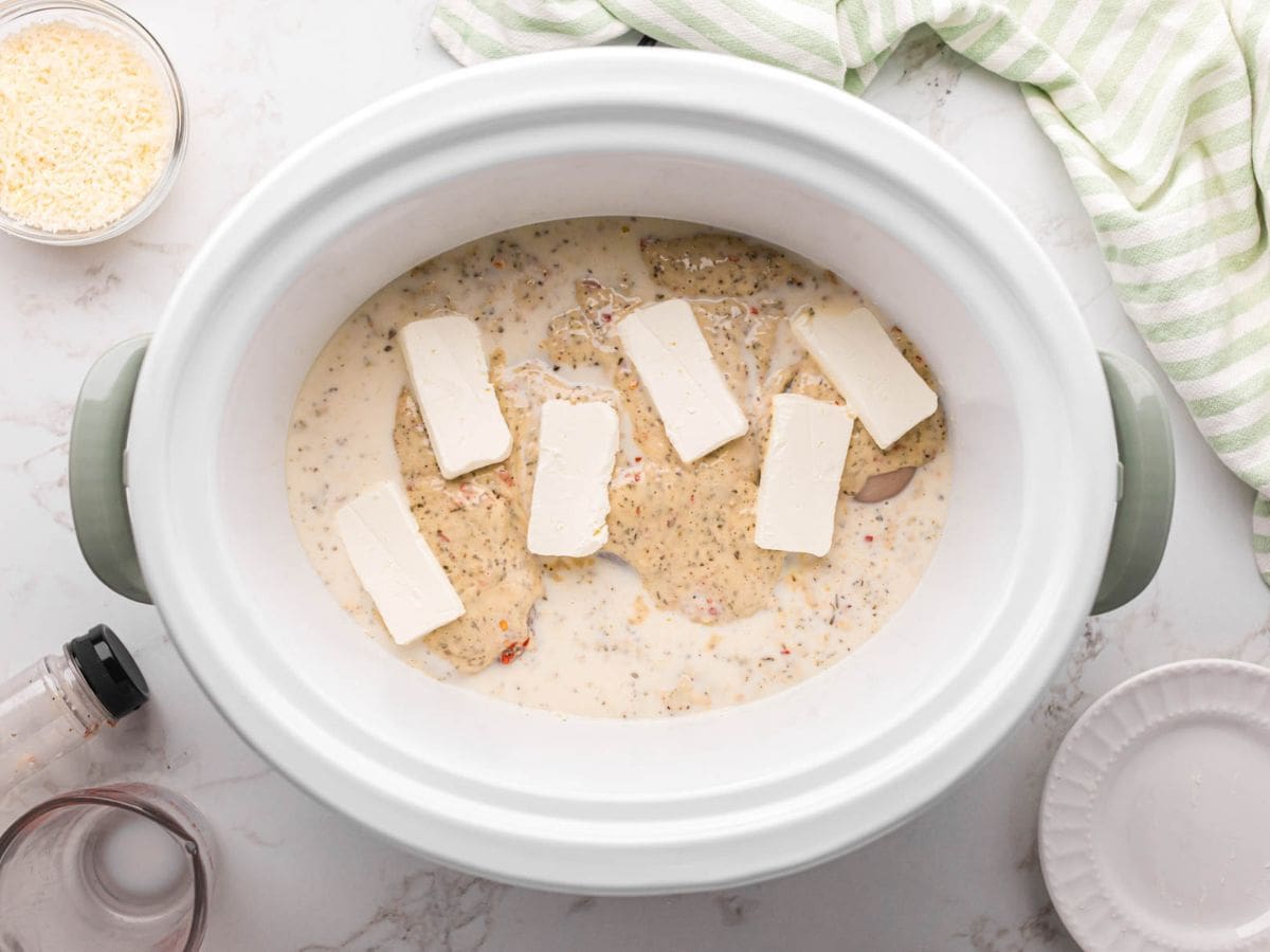 Slices of cream cheese laid over chicken and sauce in the crockpot.