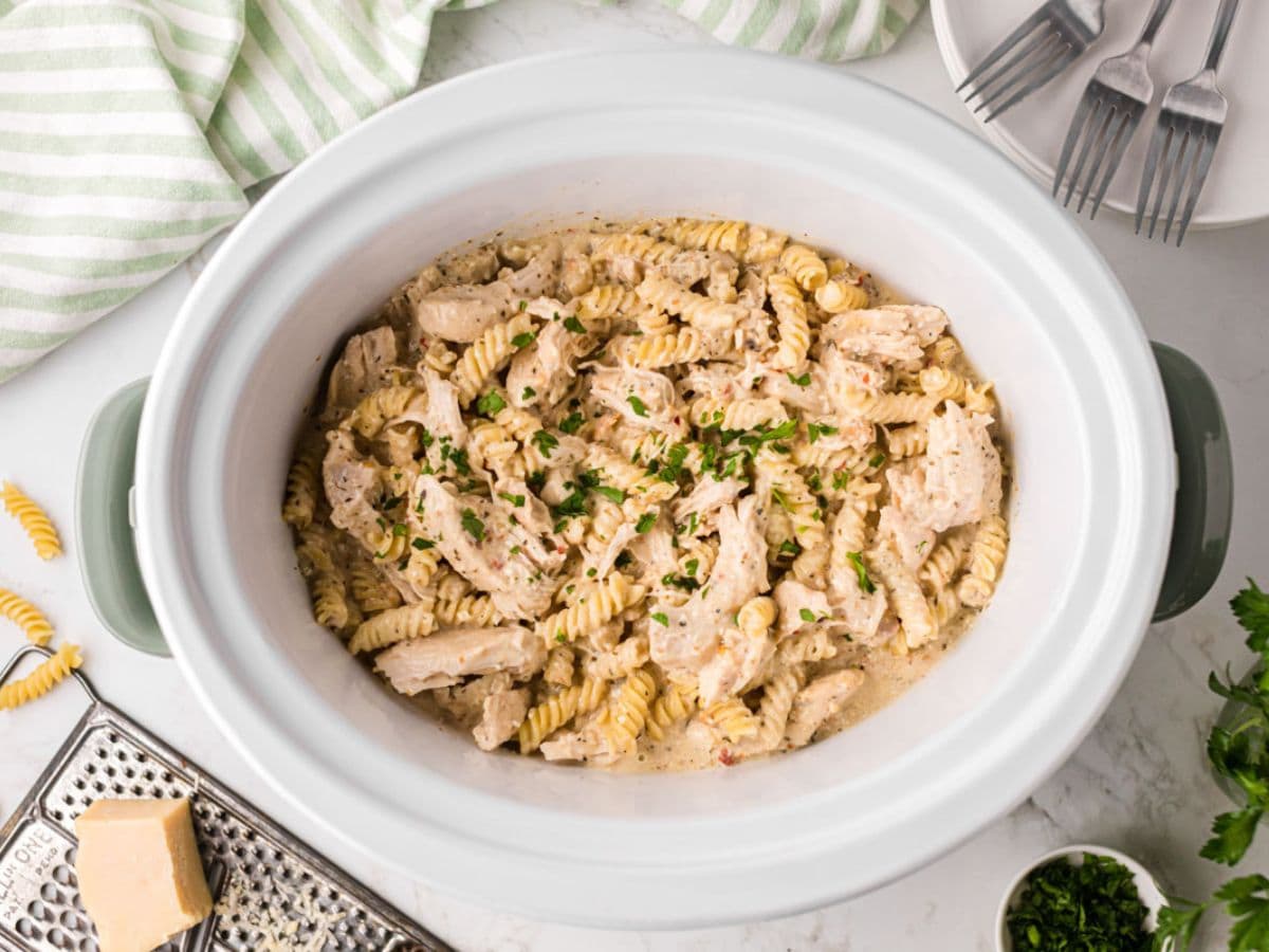 Slow cooker filled with the cooked garlic Parmesan chicken topped with parsley.