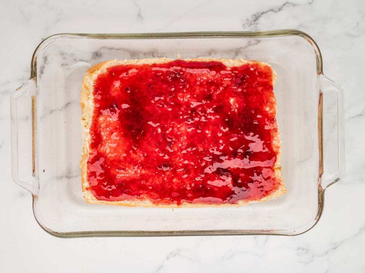 Bottom layer of bread with jam on it in a baking dish.