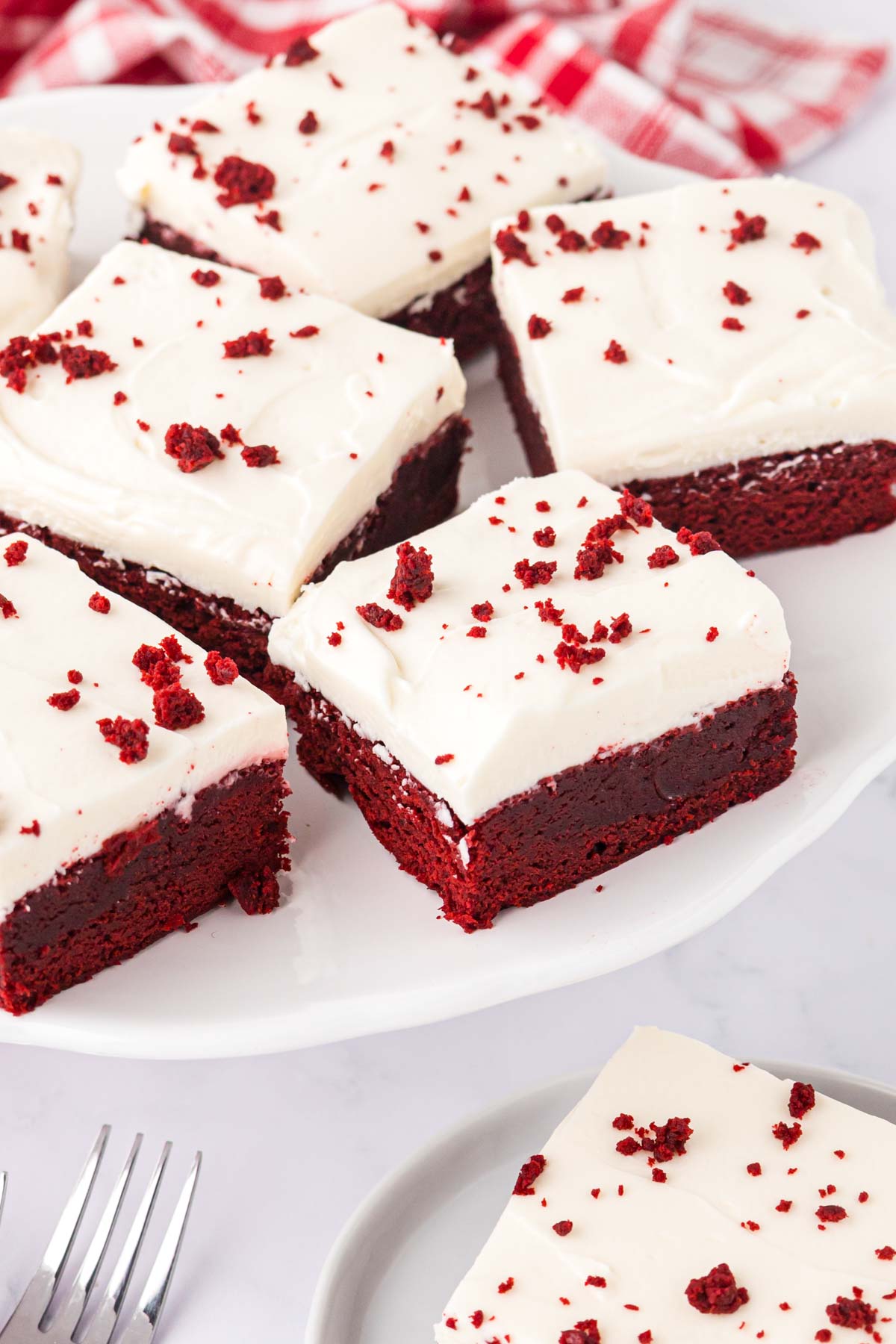 Cut red velvet brownie sliced topped with red velvet crumbs on a white serving platter.