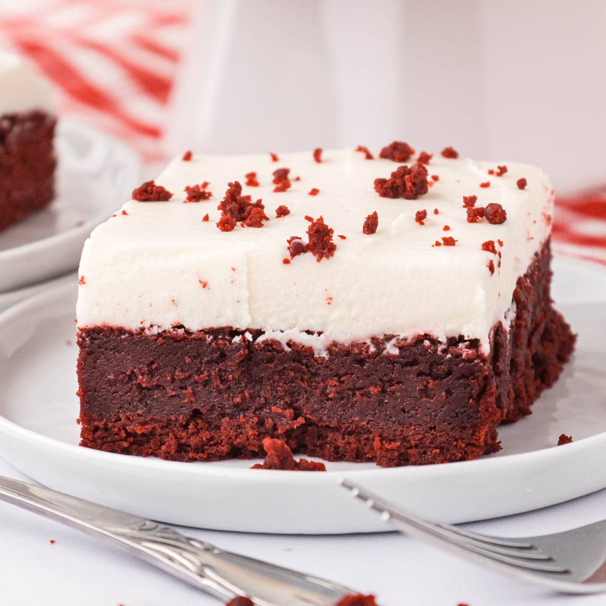 Ice red velvet brownie on a white plate topped with cream cheese icing.