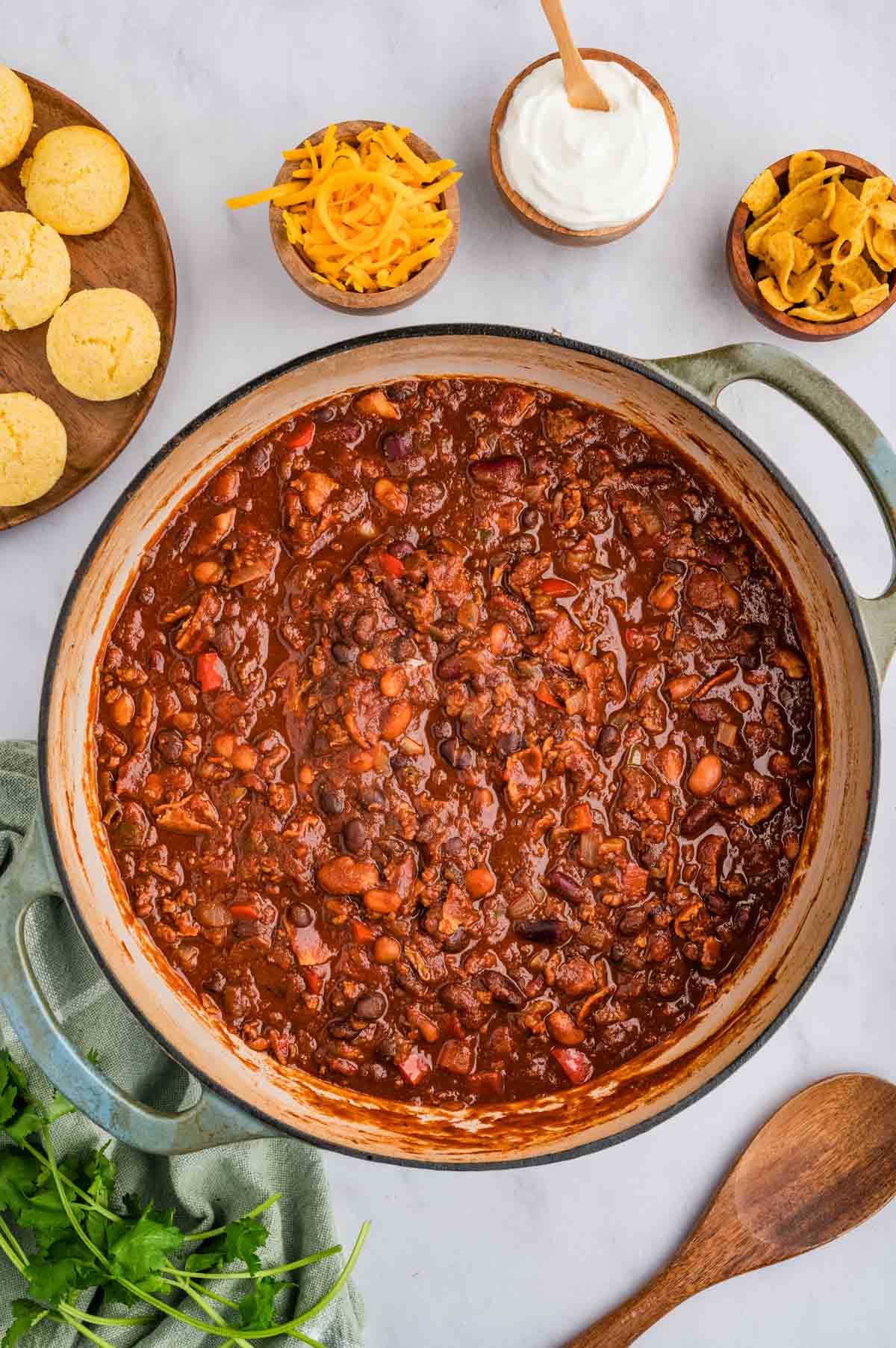 Overhead shot of smoked chili with bacon in a dutch oven with toppings placed around it.