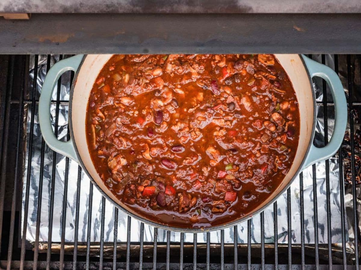 Placing the Dutch oven filled with chili on a grill to smoke.