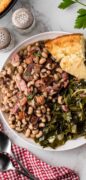 Black-eyed peas on a white plate with collard greens and cornbread.