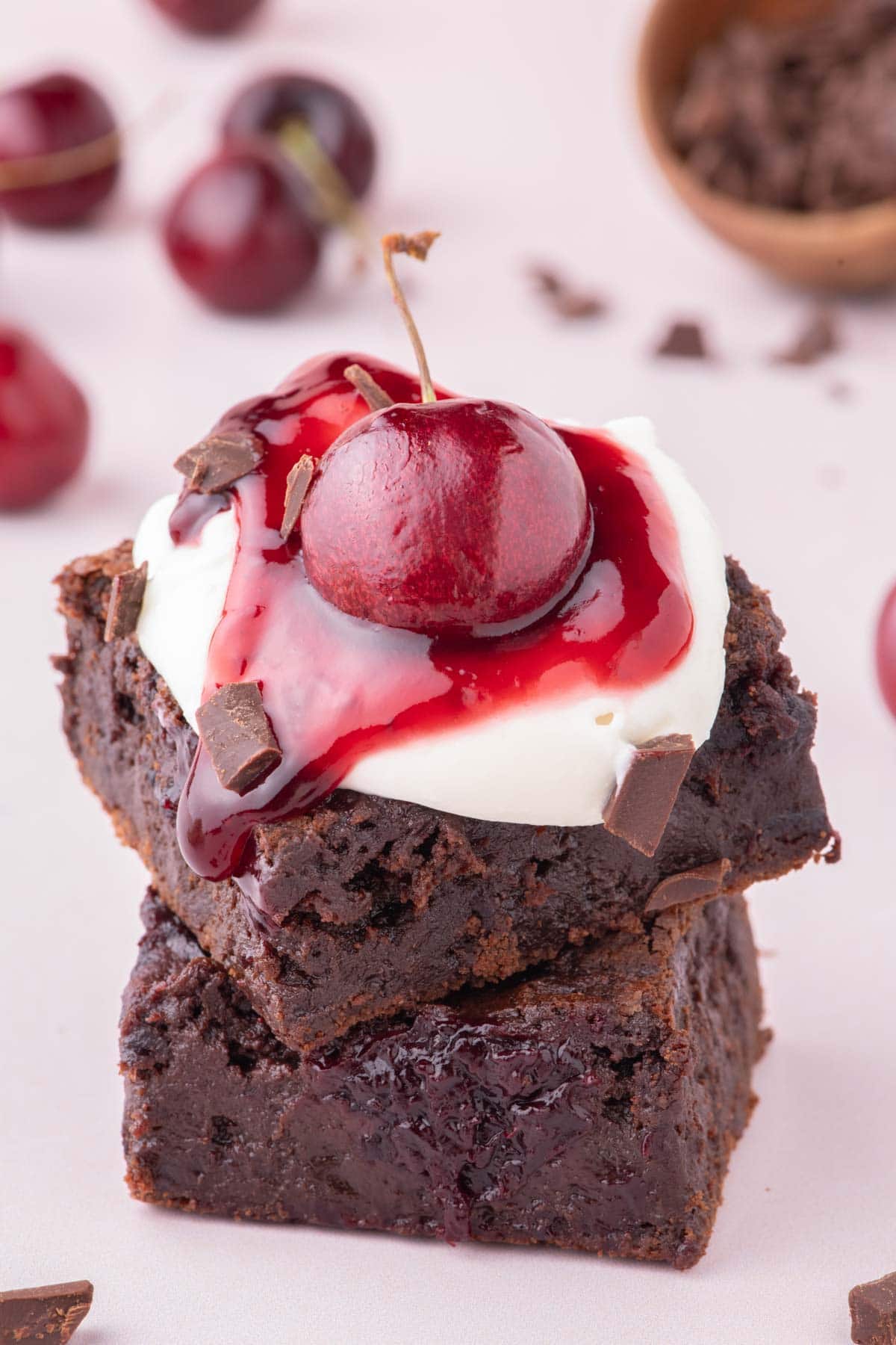 Two brownies stacked on top of each other topped with whipped topping, cherry filling, and a fresh cherry.