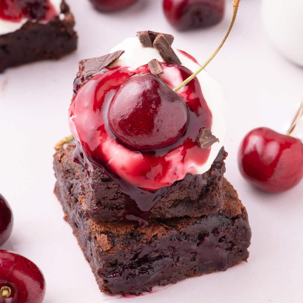 Two black forest brownies stacked on top of each other with a fresh cherry on top.