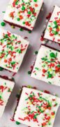 Parchment paper holds several cut red velvet Christmas brownies topped with cream cheese frosting and Christmas sprinkles.