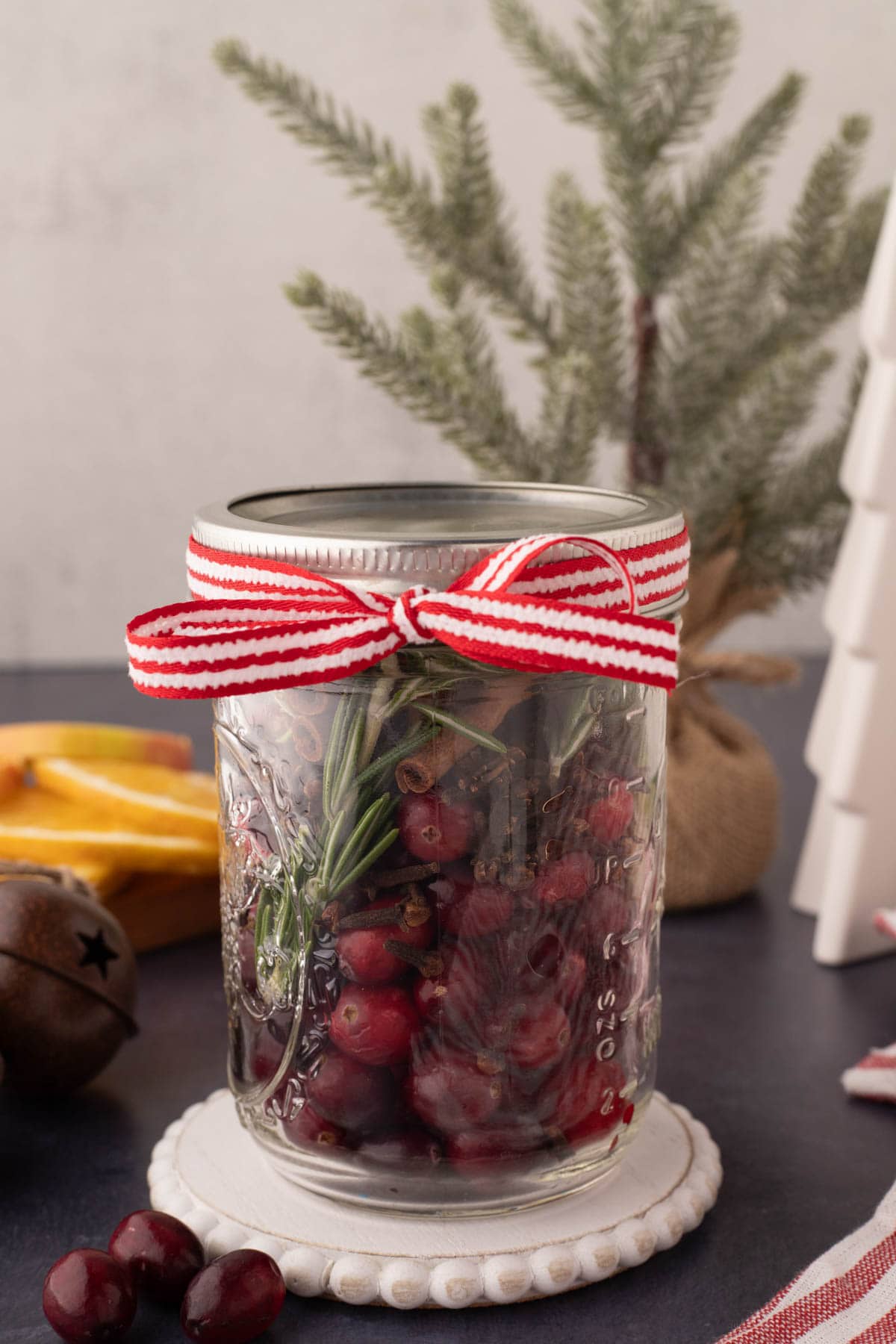 A mason jar with cranberries, cinnamon sticks, rosemary, sprigs, and cloves