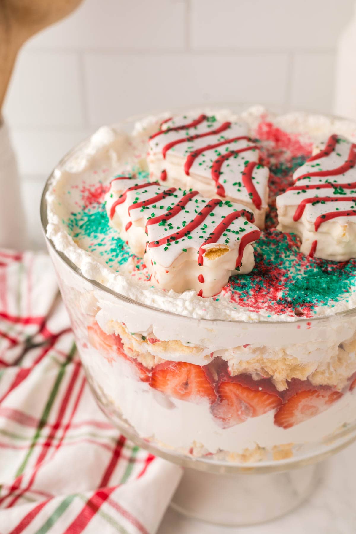 A trifle bowl filled with Christmas tree cake layers, strawberries and whipped cream.