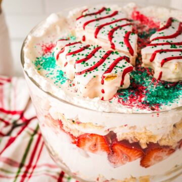 A trifle bowl filled with Christmas tree cake layers, strawberries and whipped cream.