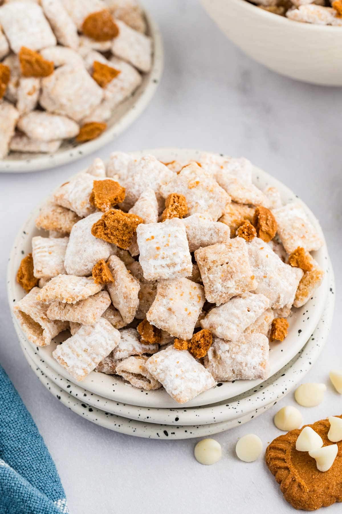 Cookie butter muddy buddies served on a stack of white plates with more in the background.