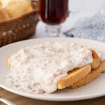 Two slices of toast on a plate with chip beef gravy on top and sprinkled with black pepper.