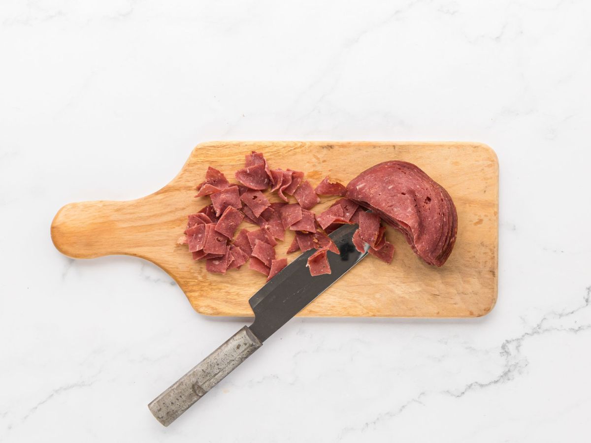 A cutting board with dried beef cut with a knife.