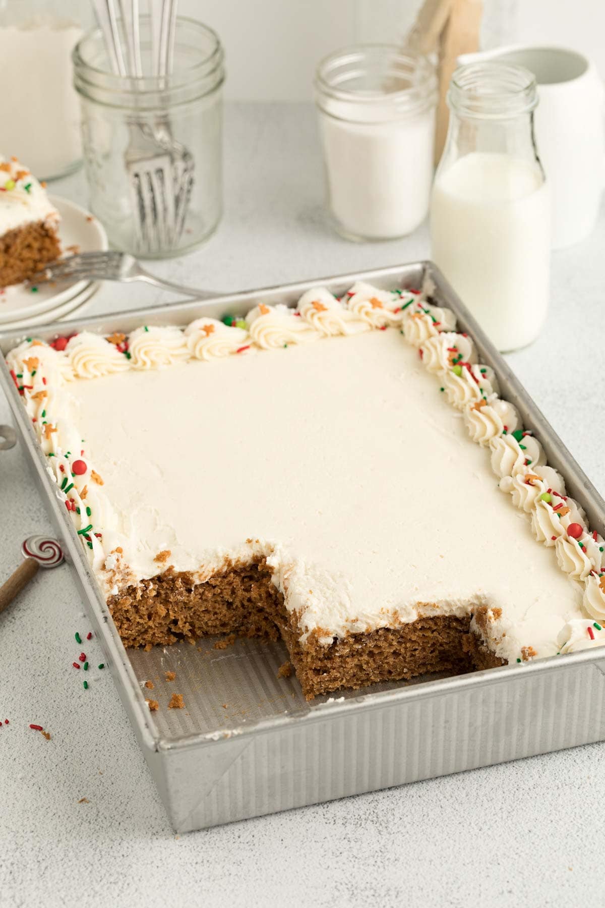 Gingerbread cake in a baking dish with some sliced missing and milk in the background.