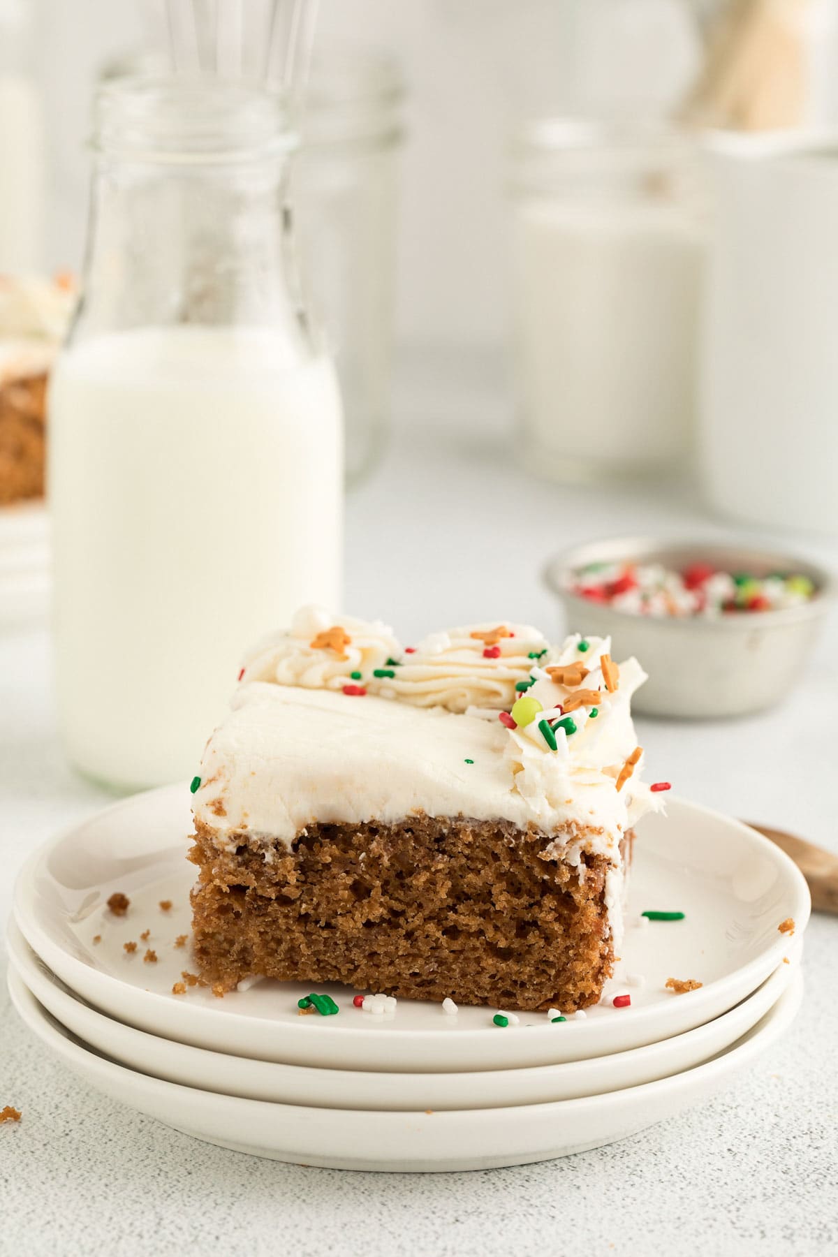 Slice of gingerbread cake on a stack of white plates with sprinkles on top.