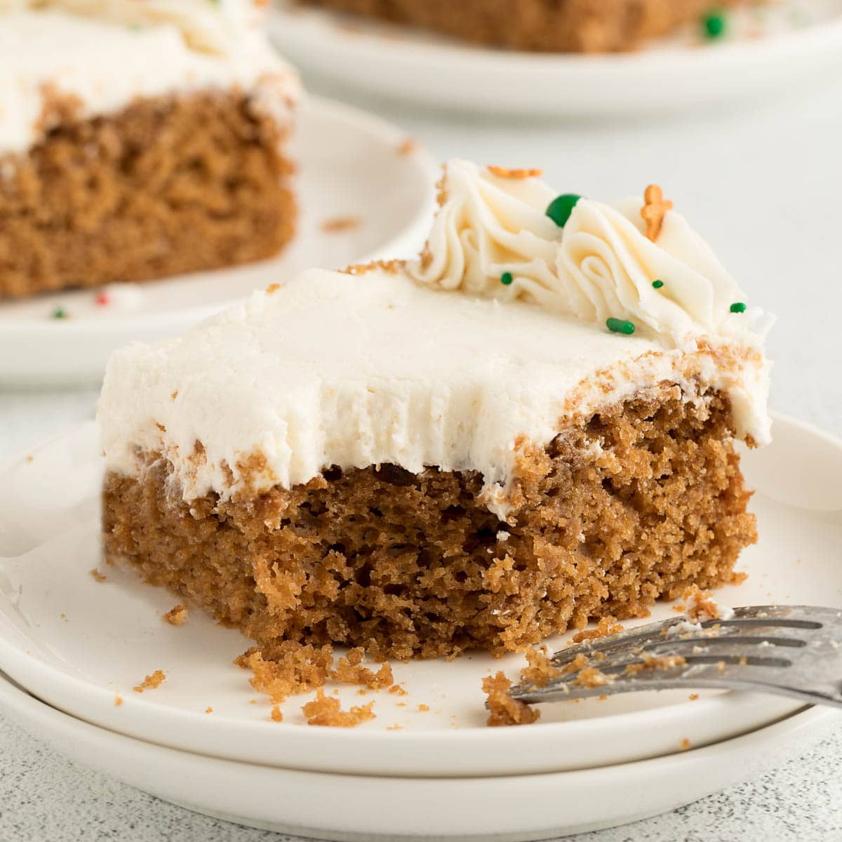 A slice of gingerbread cake with icing and gingerbread sprinkles.