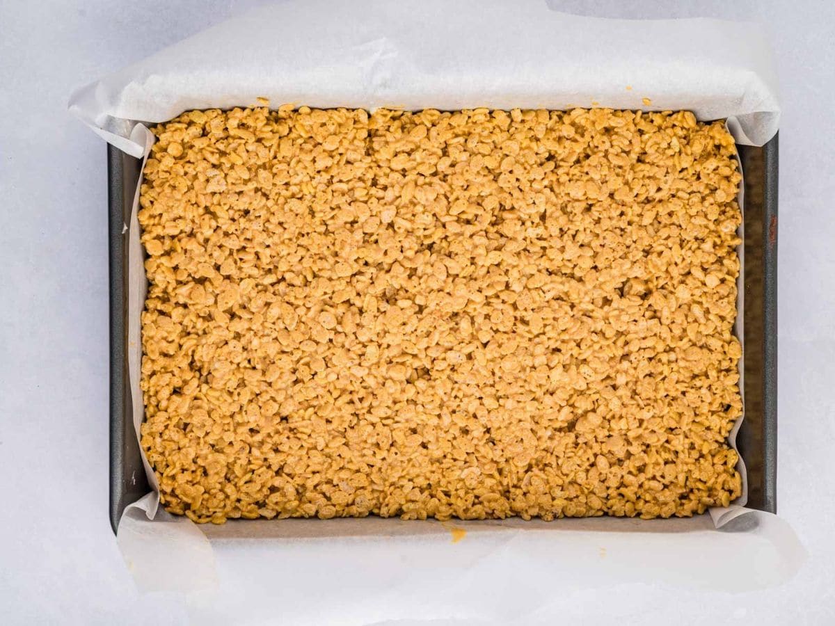 Gingerbread rice krispie mixture pushed into a baking dish in an even layer.