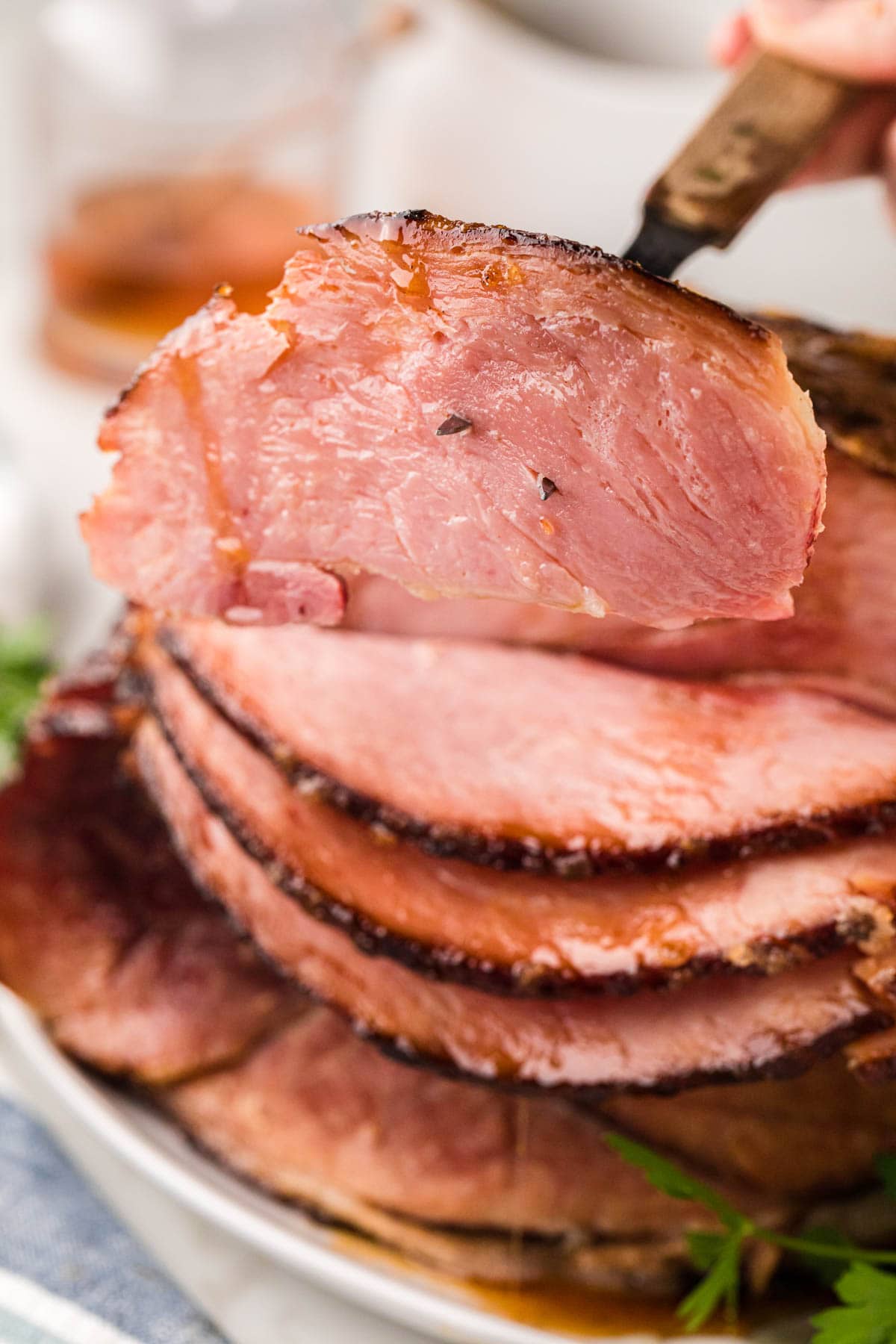 A slice of ham being built removed with a serving fork from the whole ham.