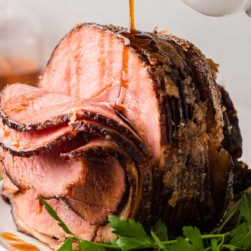 A sliced spiral ham on a white platter garnished with parsley.