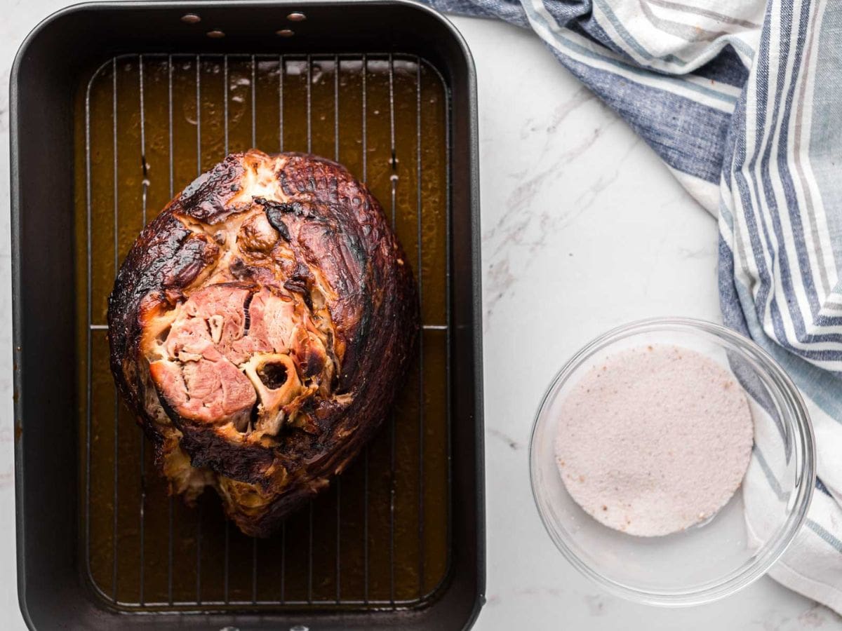 A cooked spiral ham taken out of the oven sitting in the roasting pan cooling.