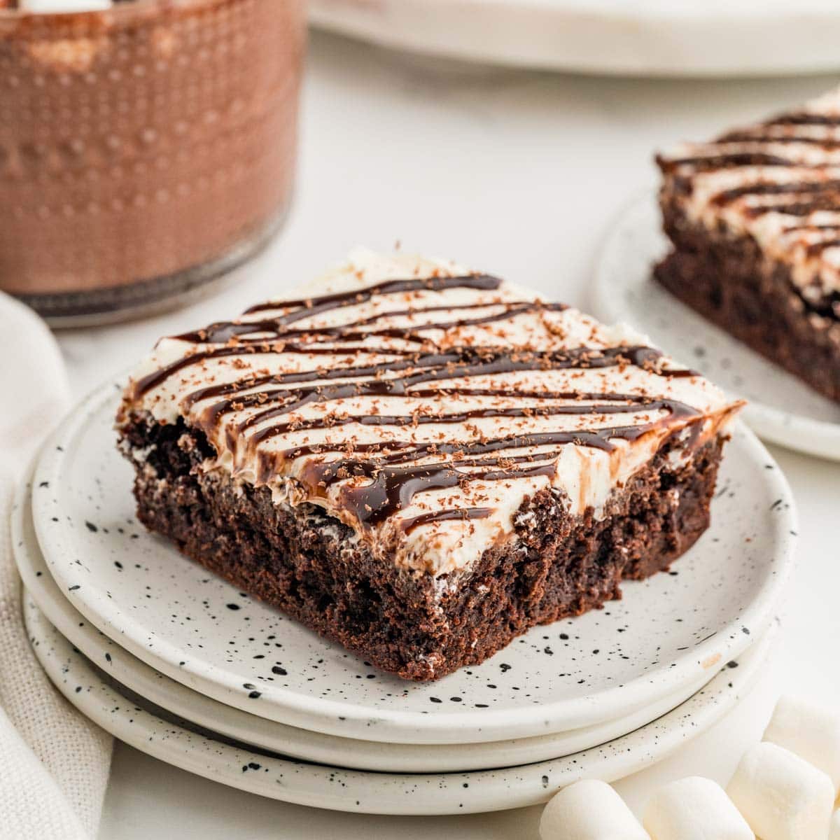 Square hot chocolate brownie on a stack of white speckled plates.