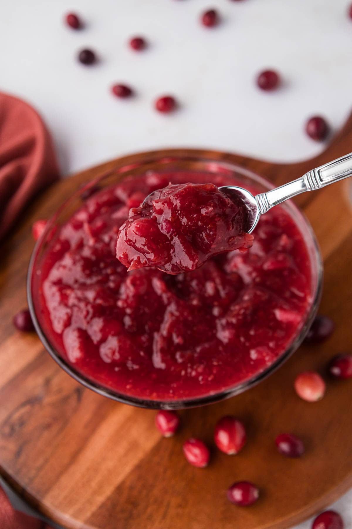 A silver spoon removing a serving of cranberry sauce from a bowl.