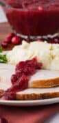 Pinterest image or instant pot cranberry sauce with the picture of the bowl of cranberry sauce in the background and a plate of sliced turkey and mashed potatoes with cranberry sauce.