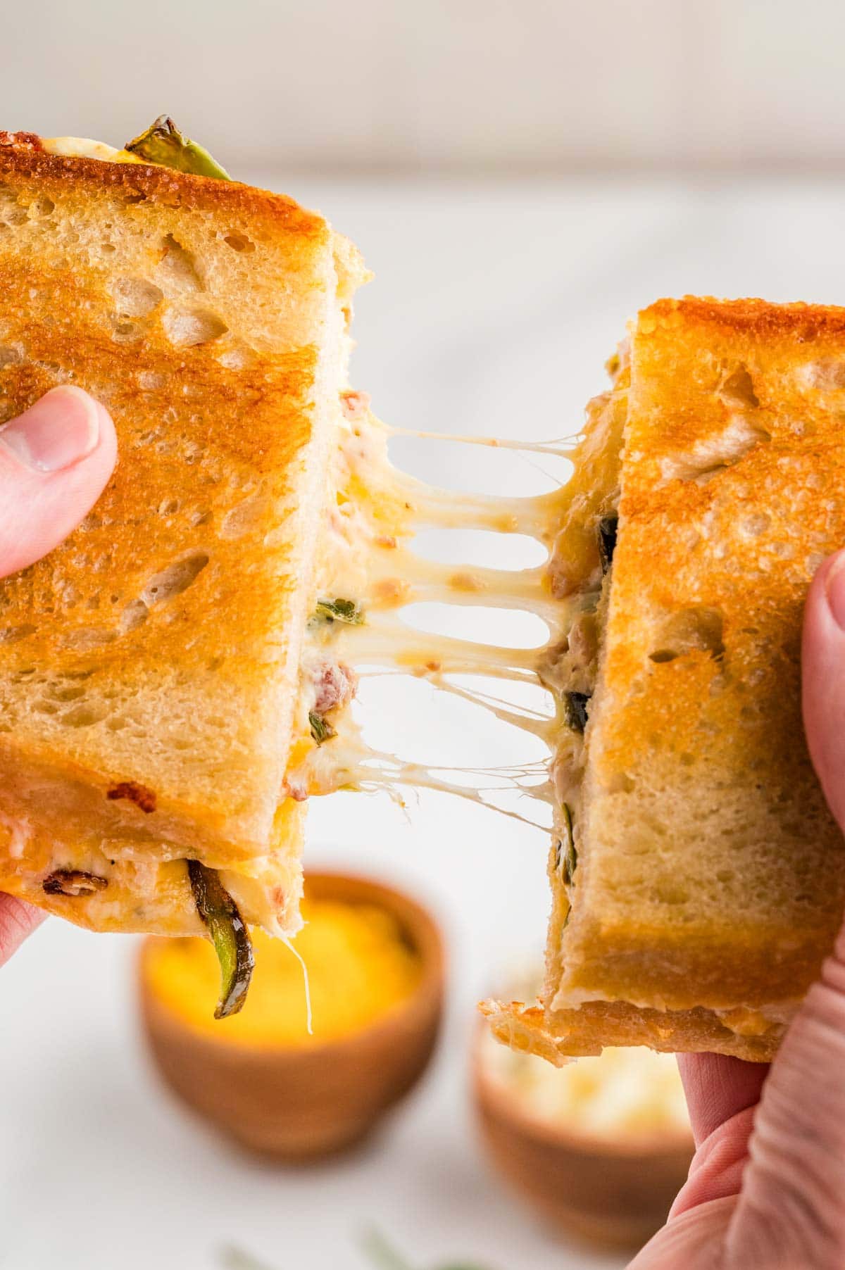 Hands pulling apart two halves of a jalapeno popper grilled cheese to show the melty cheese.