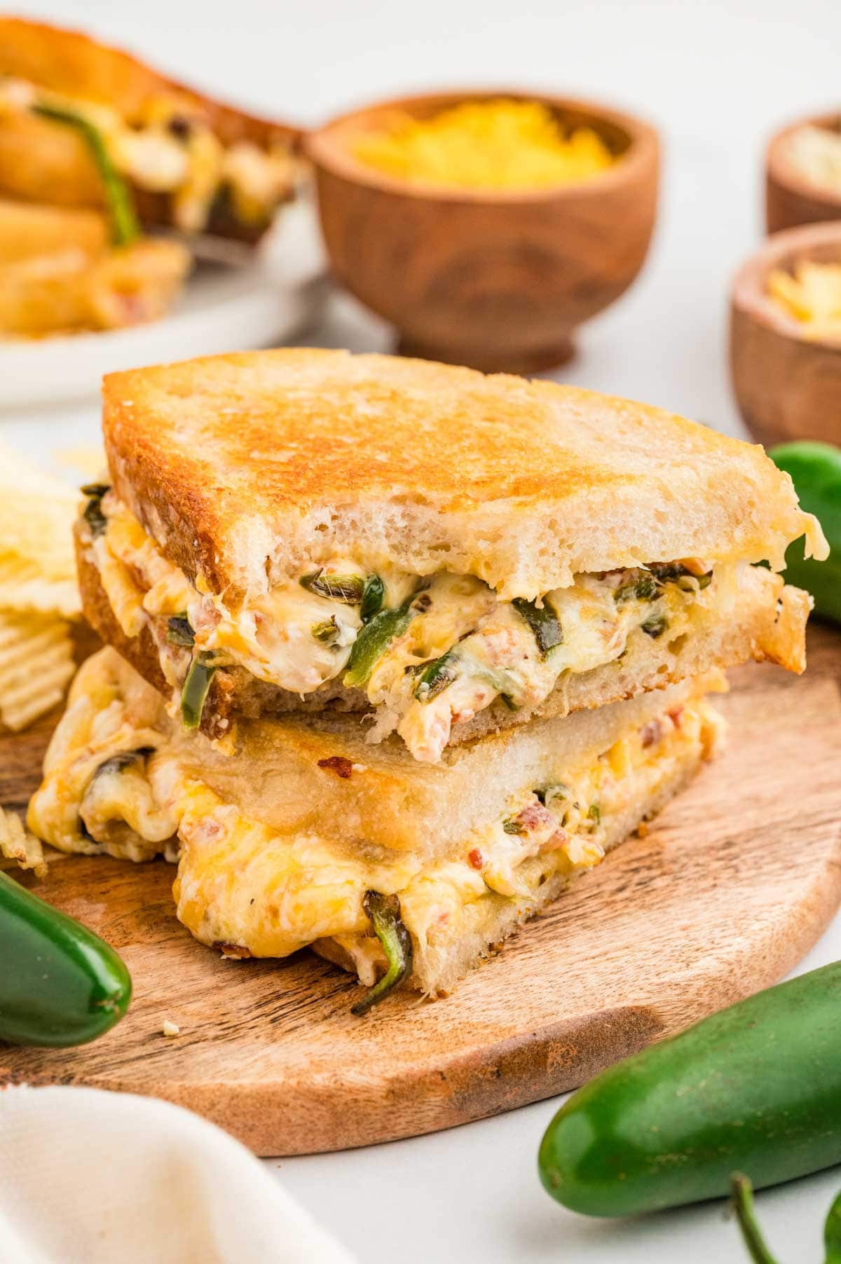 Two halves of the jalapeno popper grilled cheese stacked on top of each other on a wooden board.