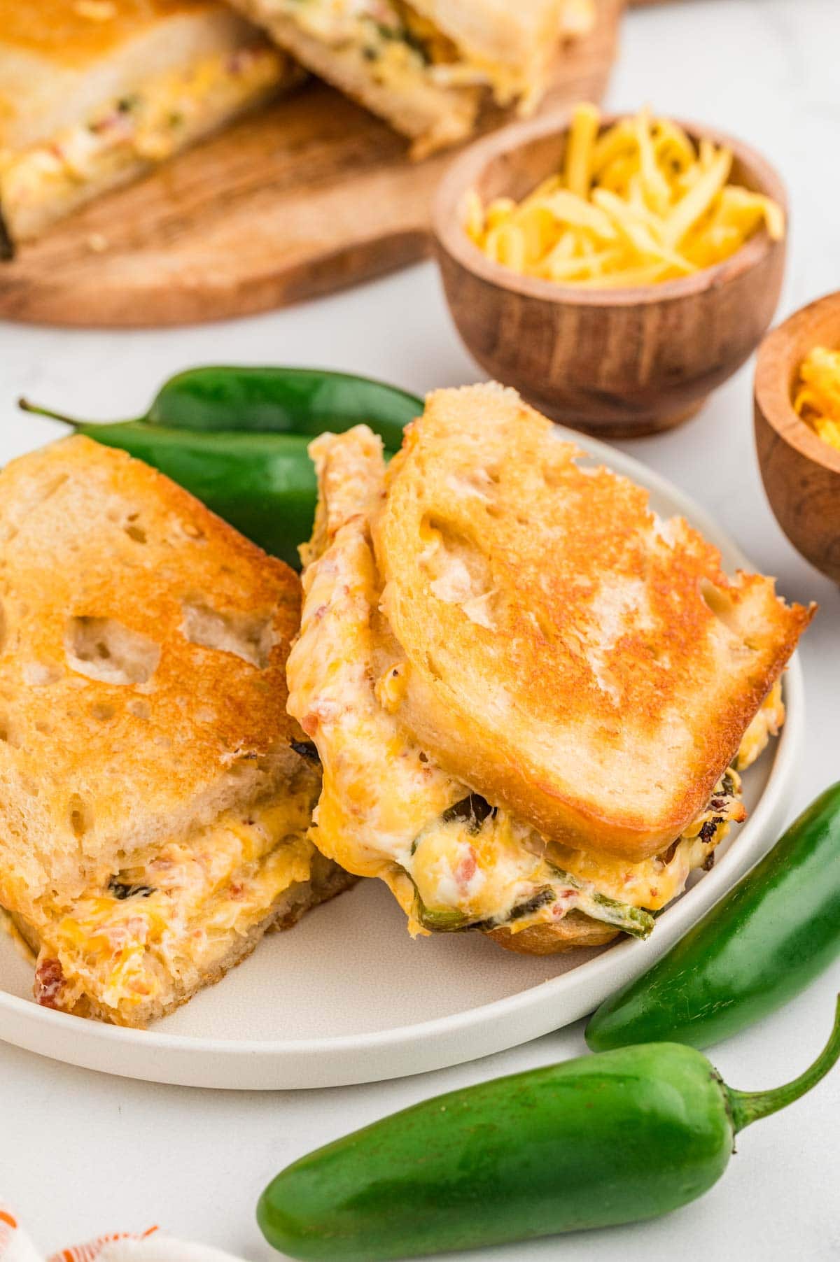 Jalapeño popper grilled cheese sliced in half on a plate with more jalapenos around it.