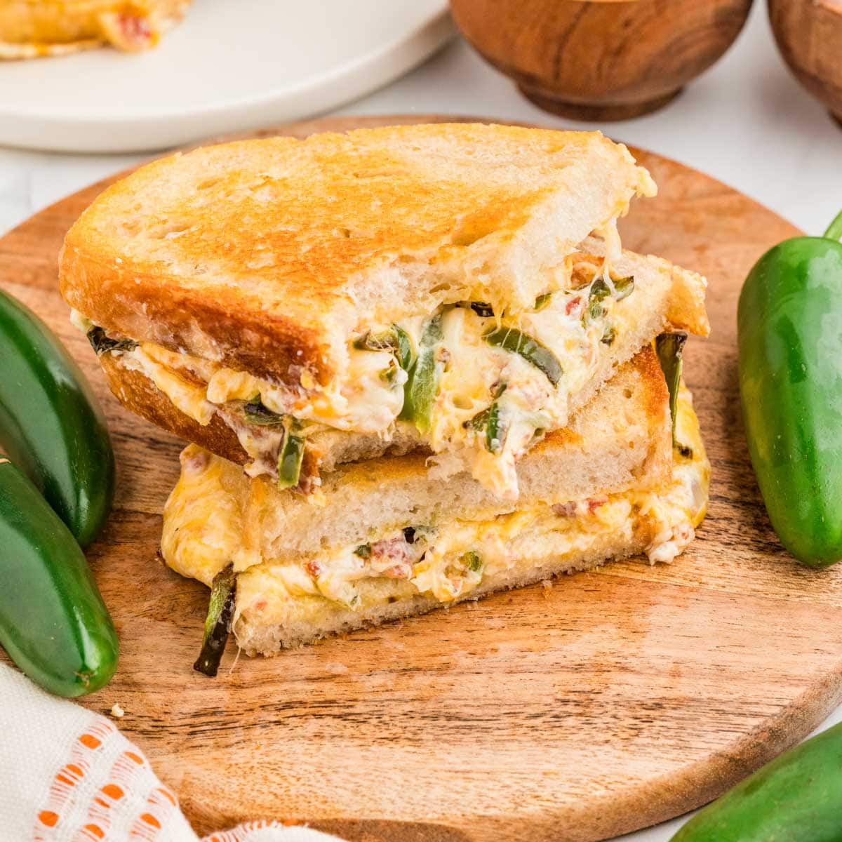 Jalapeno popper grilled cheese cut in half and stacked on top of each other on a wooden board with one bite missing.