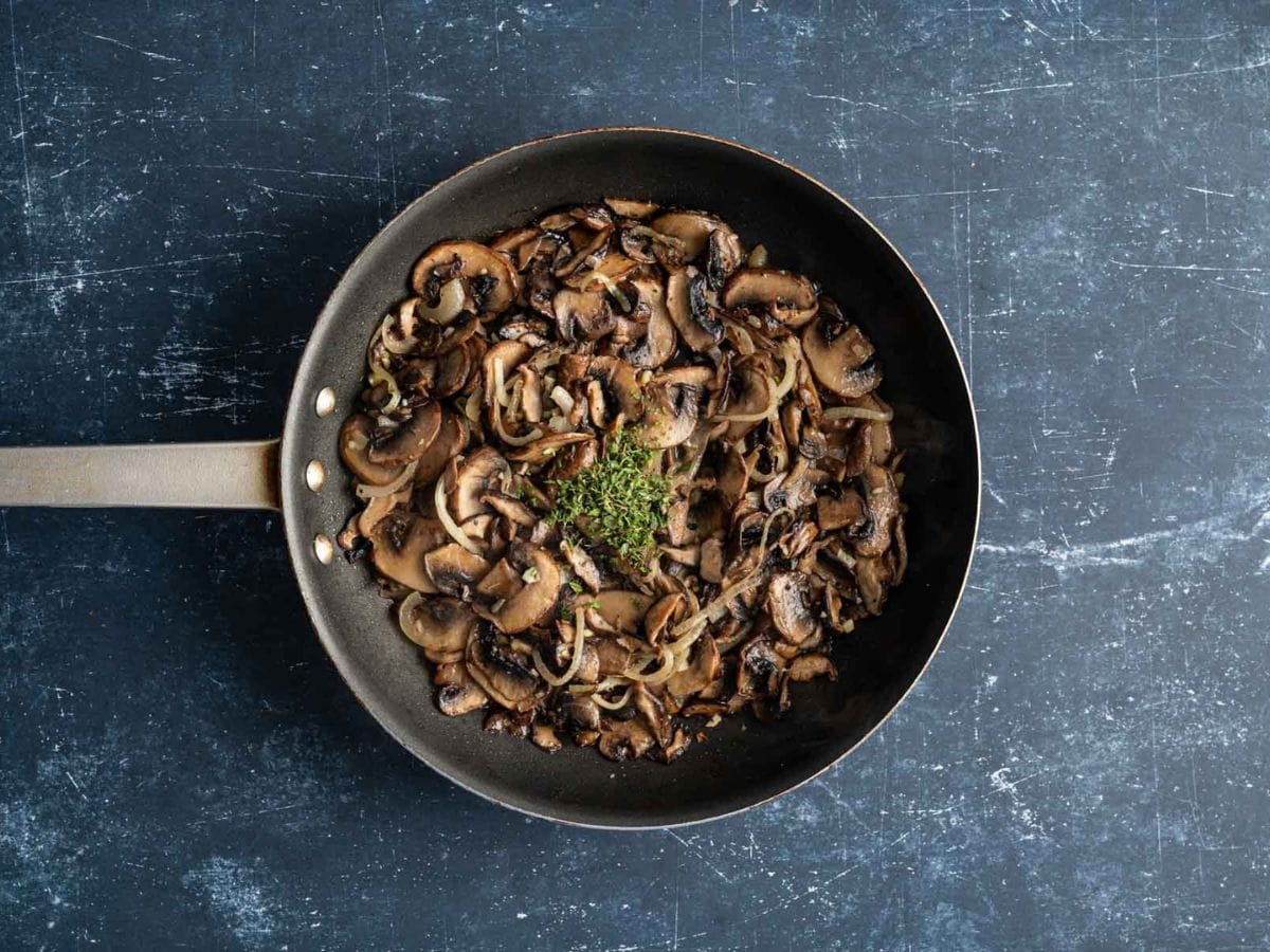 Cooked mushrooms with thyme being added in the skillet.