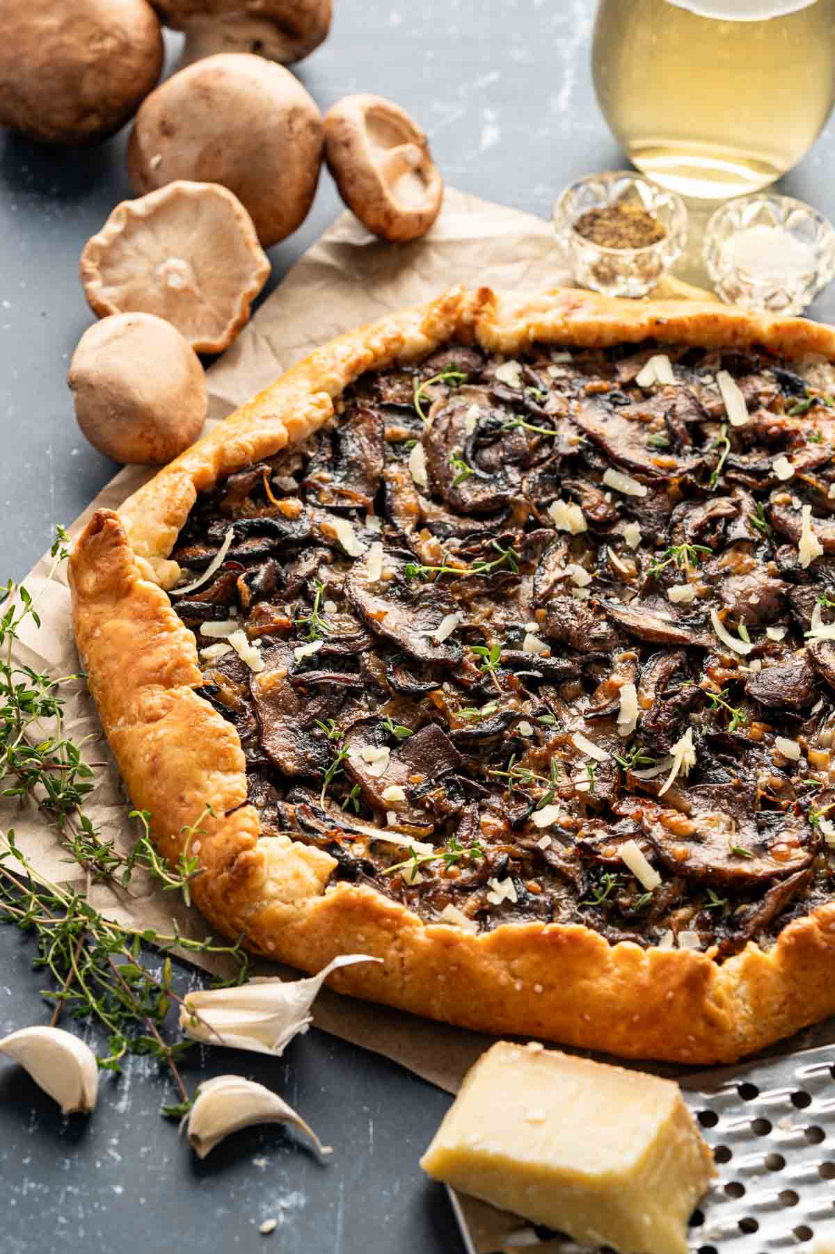 Mushroom galette served with wine and some mushrooms placed behind it.