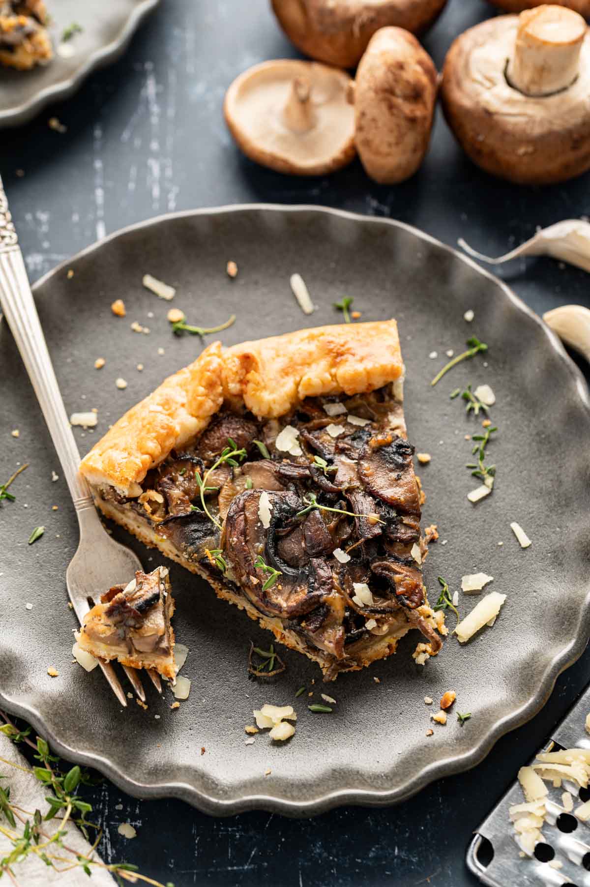 Slice of mushroom galette on a grey plate with a fork taking a bite.