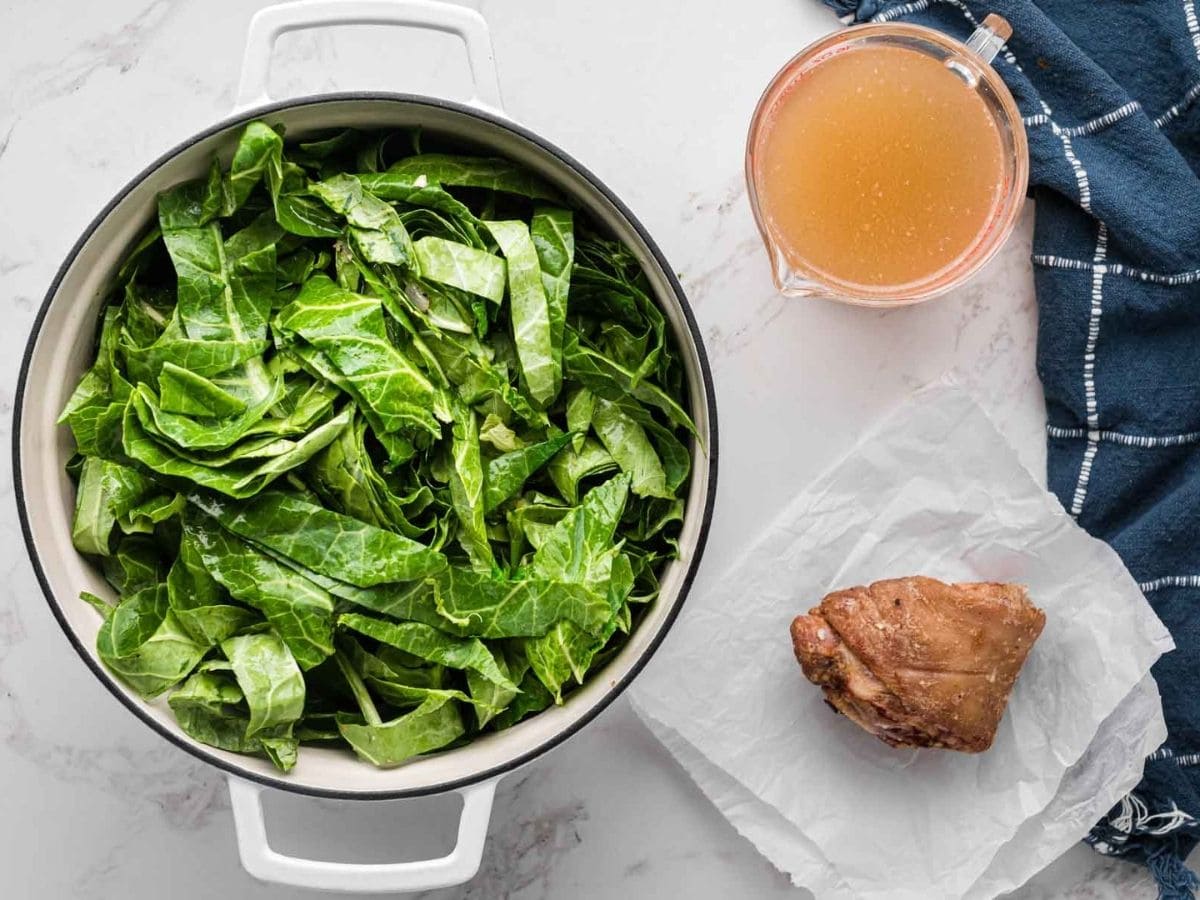 Collard greens added to a large white dutch oven.